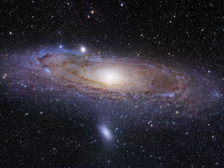 Photo of the swirling stars of the Andromeda Galaxy shown in purples, yellows, and reds against black background.